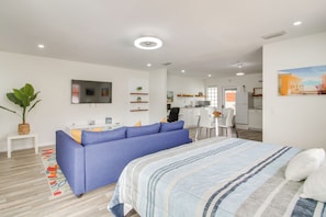 En moderne stue med sofa, seng, et fladskærms-TV, et spiseområde og et køkken i baggrunden.