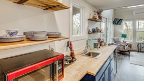 A modern kitchen with a red microwave, wooden shelves, a sink, and a dining area with patterned chairs. - Nature Stay By Guntersville Lake! Cozy Guest Cabin (Grant)