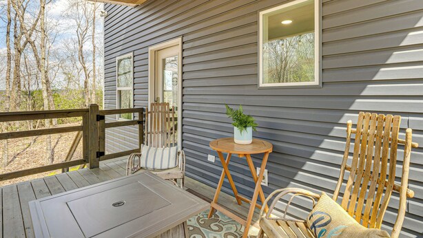 A wooden deck with a table and chairs, a small round table with a plant, and a wooden chair with a cushion. - Nature Stay By Guntersville Lake! Cozy Guest Cabin (Grant)