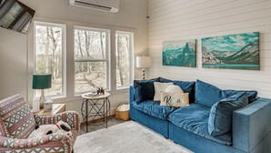 A living room with a blue sofa, patterned armchair, and a view through large windows. - Nature Stay By Guntersville Lake! Cozy Guest Cabin (Grant)