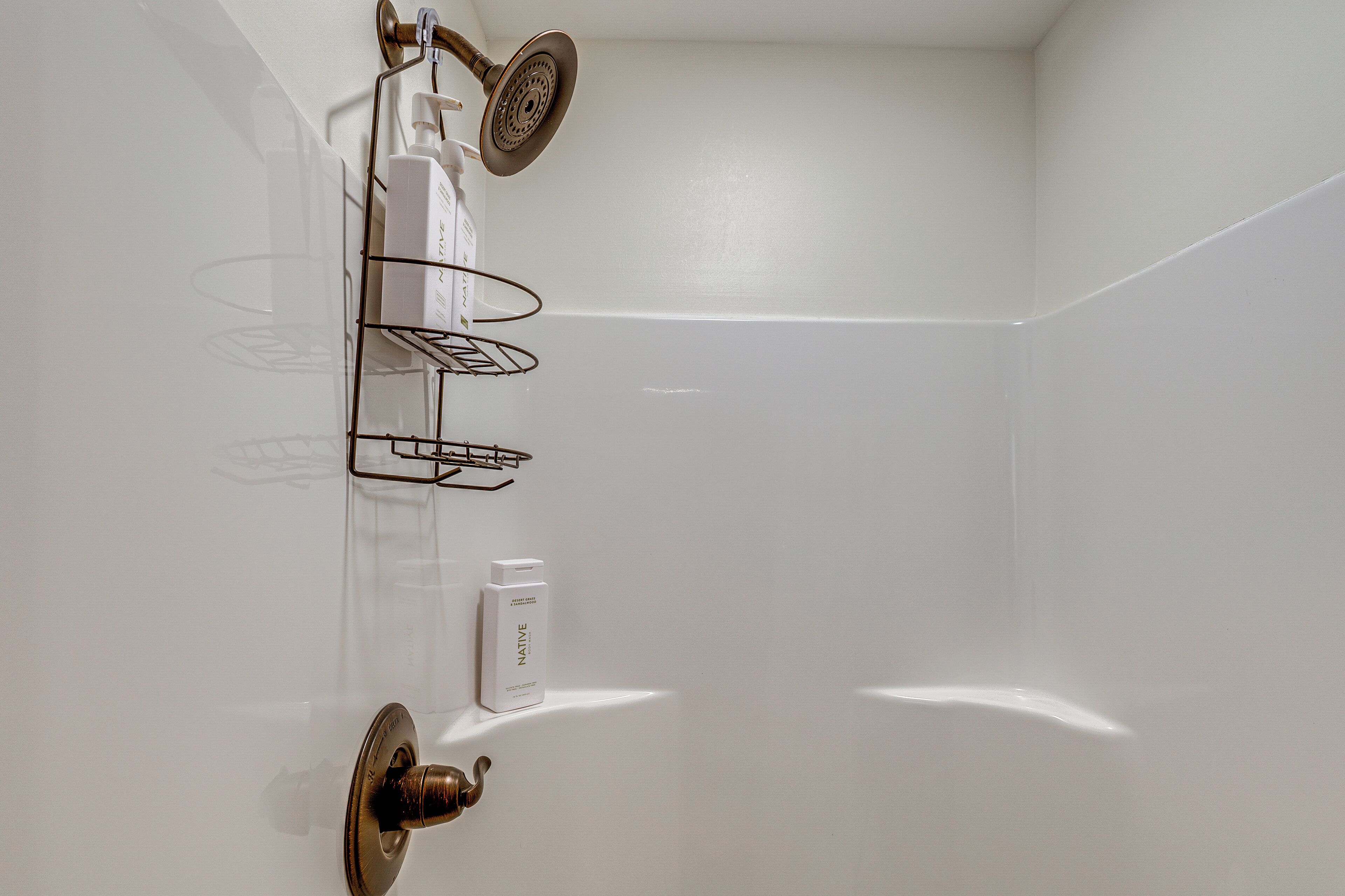 Un baño con pared de azulejos blancos, ducha con cabezal de ducha manual, toallero y dispensador de jabón.