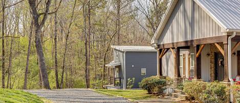 A two-story building with a porch, a gravel driveway, and a forested backdrop.
