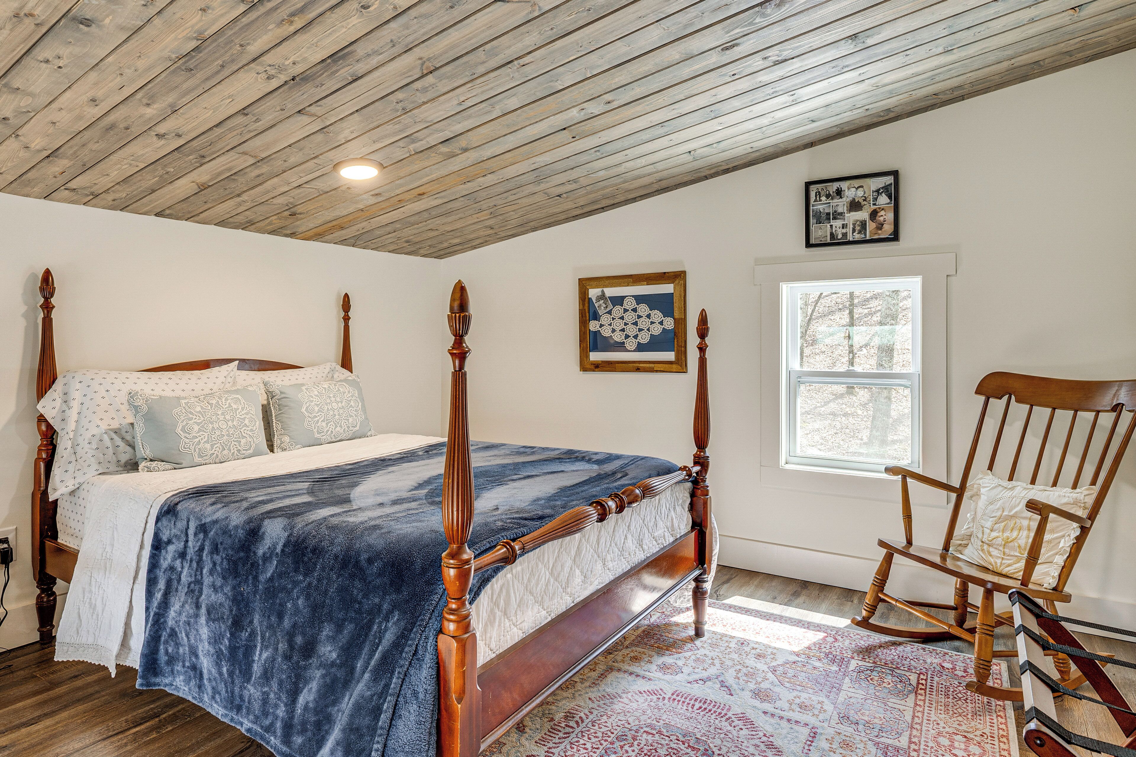 Une chambre à coucher avec un lit à baldaquin, un fauteuil à bascule, une fenêtre et un tableau encadré au mur.