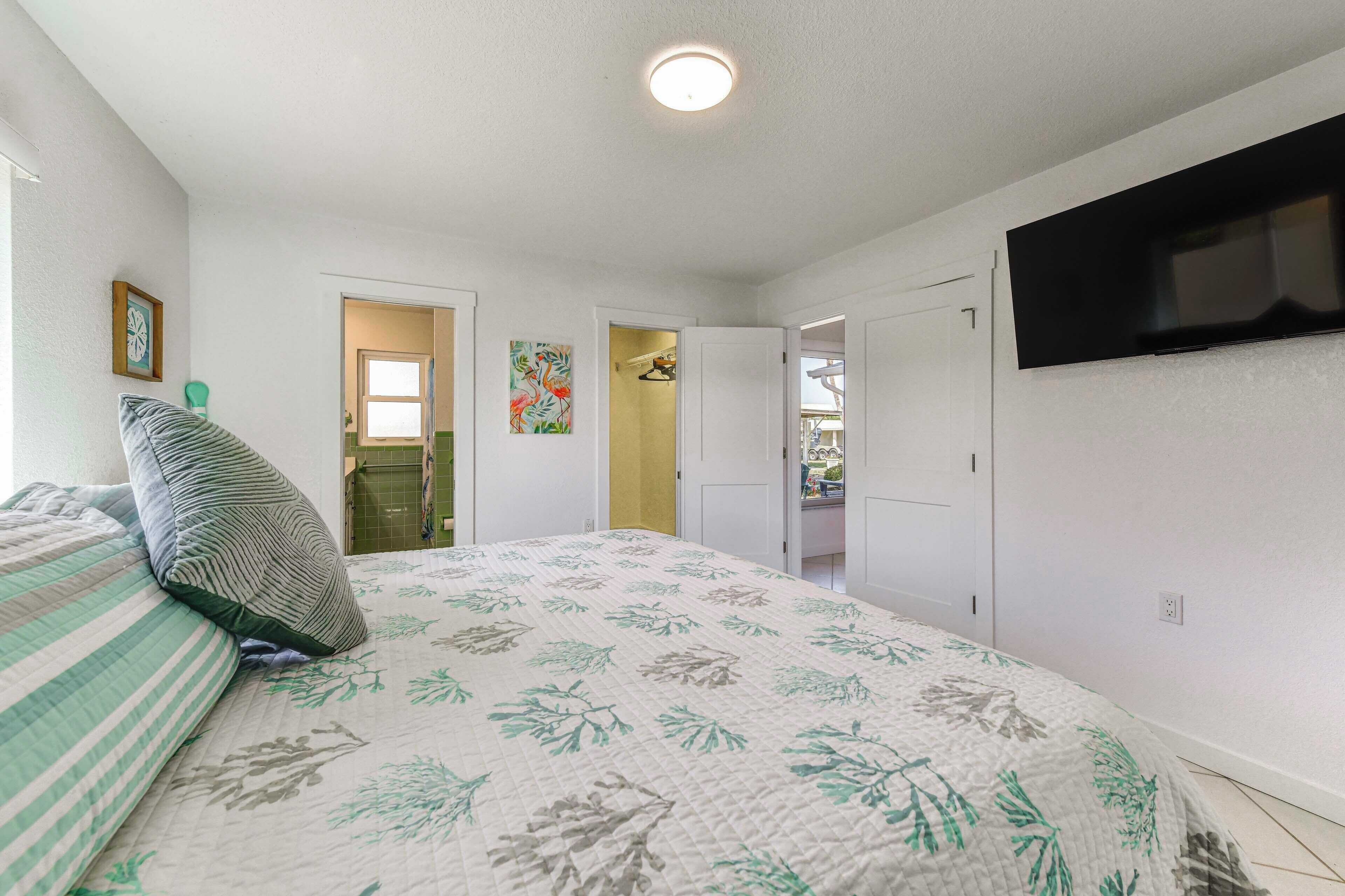 Ein Schlafzimmer mit einem Bett, einem an der Wand befestigten Fernseher und einer Tür zu einem Badezimmer.