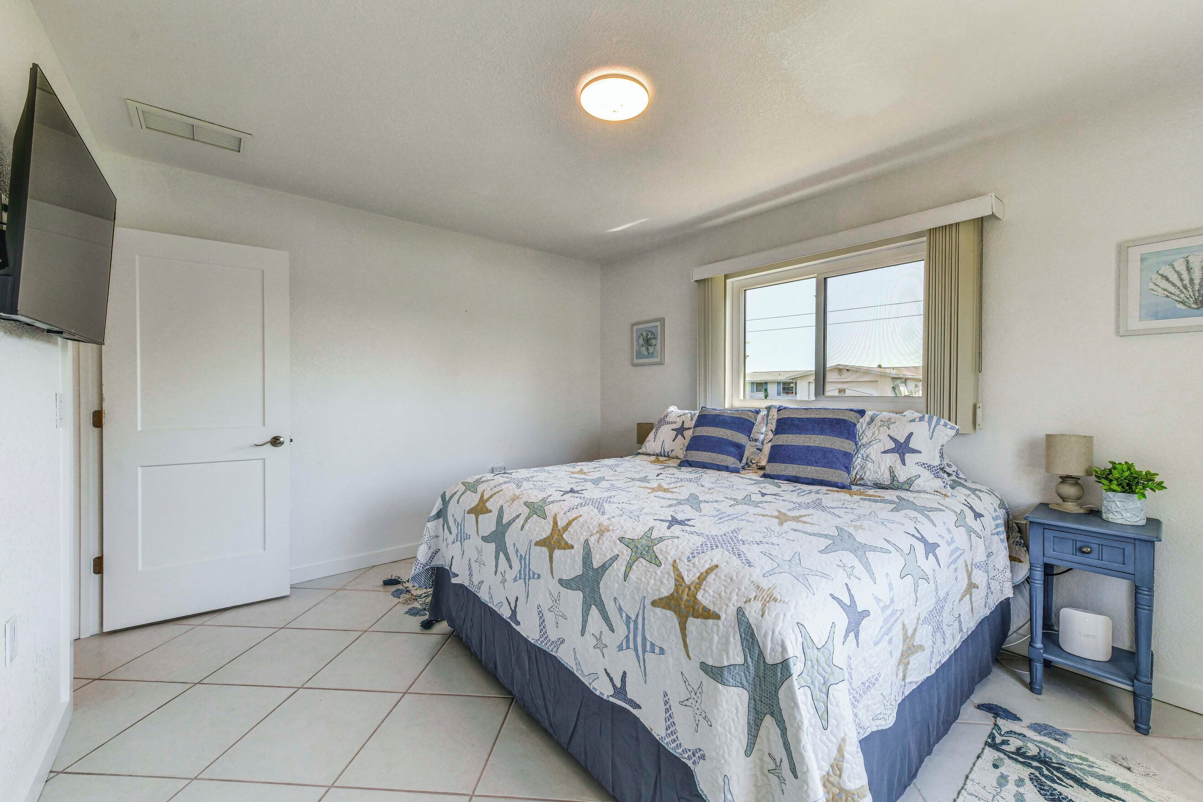 A bedroom with a bed, a window, a nightstand, and a door.