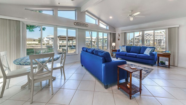 A spacious living area with a blue sofa, a dining table with chairs, and large windows offering views of the beach and buildings. - 2 Mi to Englewood Beach! Home w/ Private Dock (Englewood)