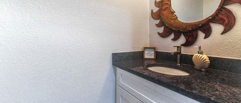 Een badkamer met een wastafel, spiegel en een bordje met de tekst over het gebruik van toiletpapier.