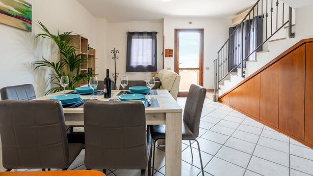 A dining area with a table set for four, a staircase, and a view of the outside. - Casa Ale Villasimius: Cozy Two-Level Home for 4 Guests Near Beaches and Services (Villasimius)