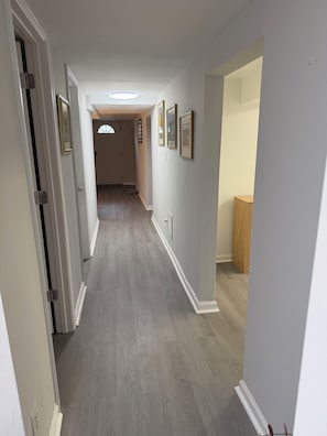 Un pasillo con piso de madera, paredes blancas y cuadros enmarcados. Hay una puerta a la izquierda y un armario a la derecha.