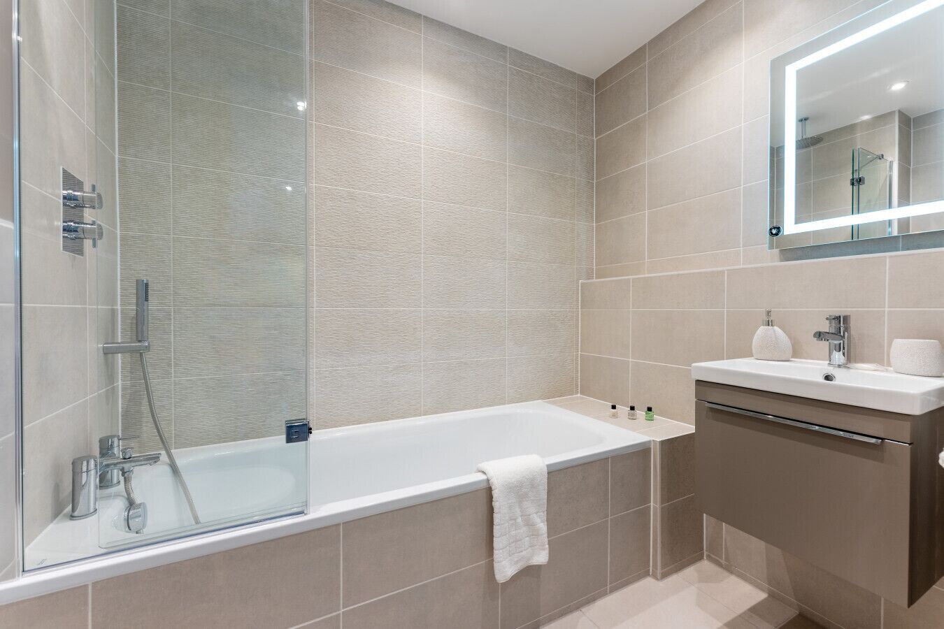 A modern bathroom with a glass-enclosed shower, a white bathtub, and a vanity with a mirror.