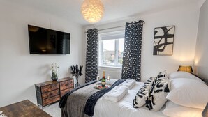 A bedroom with a bed, a dresser, a TV, a window with curtains, and a wall art piece. - The Catalina Breeze - By the harbour, park and town with parking (Dorset)