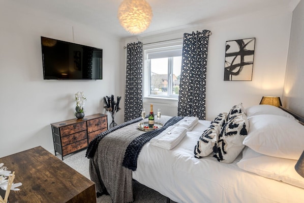 A bedroom with a bed, a dresser, a TV, a window with curtains, and a wall art piece.