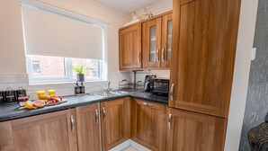 A kitchen with wooden cabinets, a sink, a toaster, and a window with a plant. - The Catalina Breeze - By the harbour, park and town with parking (Dorset)
