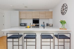 A modern kitchen with a central island, bar stools, and a decorative clock.