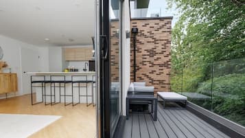 A modern kitchen with a bar area, a dining table with chairs, and a balcony with outdoor seating.