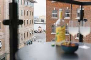 Uma mesa com uma garrafa e copos, vista de um edifício de tijolos e uma área coberta com pessoas.