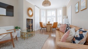 A modern living room with a sofa, chairs, a glass coffee table, a fireplace, and large windows. - Pottery Place - Close to shops, restaurants & the beach sleeps 8 (Poole)