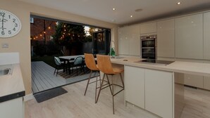 A modern kitchen with a large island, a dining area with chairs, a clock, and a view of the backyard. - Pottery Place - Close to shops, restaurants & the beach sleeps 8 (Poole)