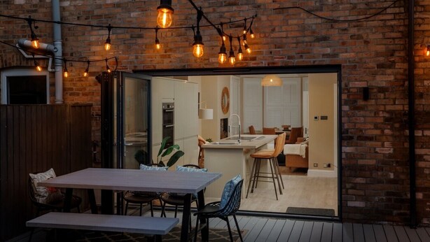 An outdoor patio with a table and chairs, a brick wall, and string lights. - Pottery Place - Close to shops, restaurants & the beach sleeps 8 (Poole)