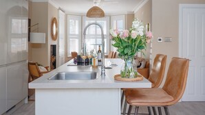 A modern kitchen with a central island, a dining area with chairs, and a vase of flowers on the island. - Pottery Place - Close to shops, restaurants & the beach sleeps 8 (Poole)