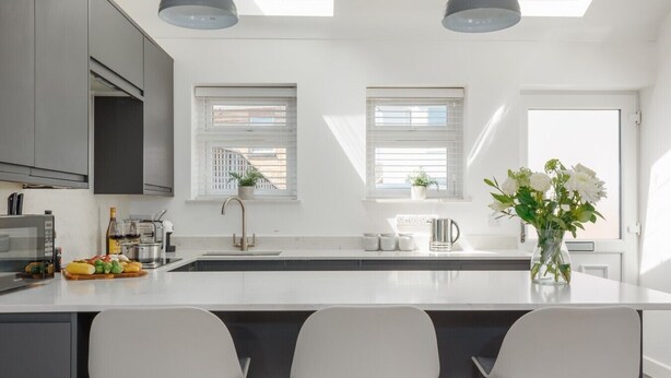 A modern kitchen with a central island, two pendant lights, and a view of the city through the windows. - Tower Hide - 1 bed with parking (Boscombe)