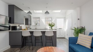 A modern kitchen with a central island, bar stools, a blue sofa, and a wooden coffee table. - Tower Hide - 1 bed with parking (Boscombe)