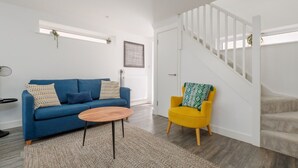 A living room with a blue sofa, a yellow armchair, a wooden coffee table, and a staircase. - Tower Hide - 1 bed with parking (Boscombe)