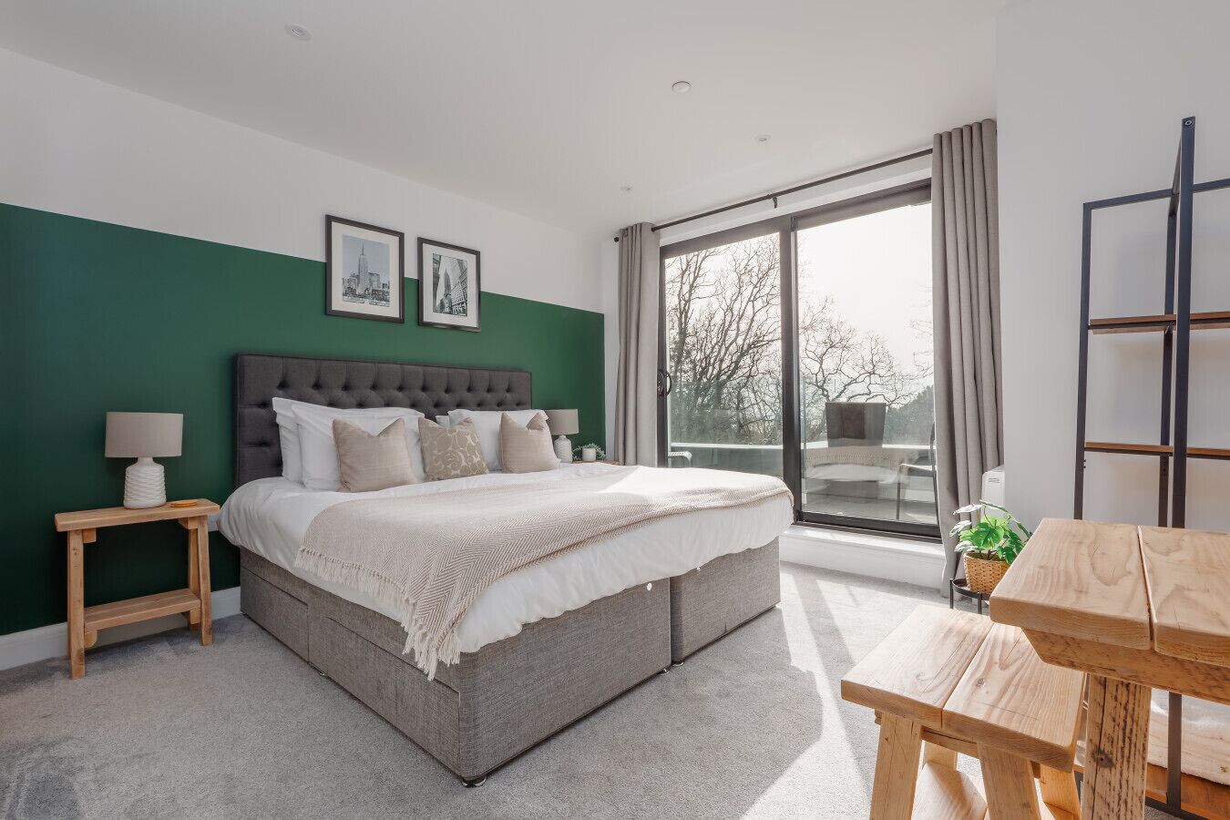 A bedroom with a large bed, a wooden nightstand, a bedside table, a window with a view, and a wooden table.
