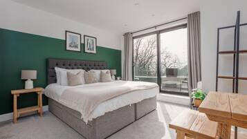 A bedroom with a large bed, a wooden nightstand, a bedside table, a window with a view, and a wooden table.
