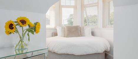 Un dormitorio con cama redonda, tocador de cristal y un florero con girasoles.
