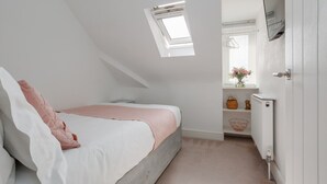 A bedroom with a sloped ceiling, a skylight, a bed with white and pink bedding, a radiator, and a small window with a basket and a figurine. - Park Views - Great for places to eat and getting to the beach (Poole)