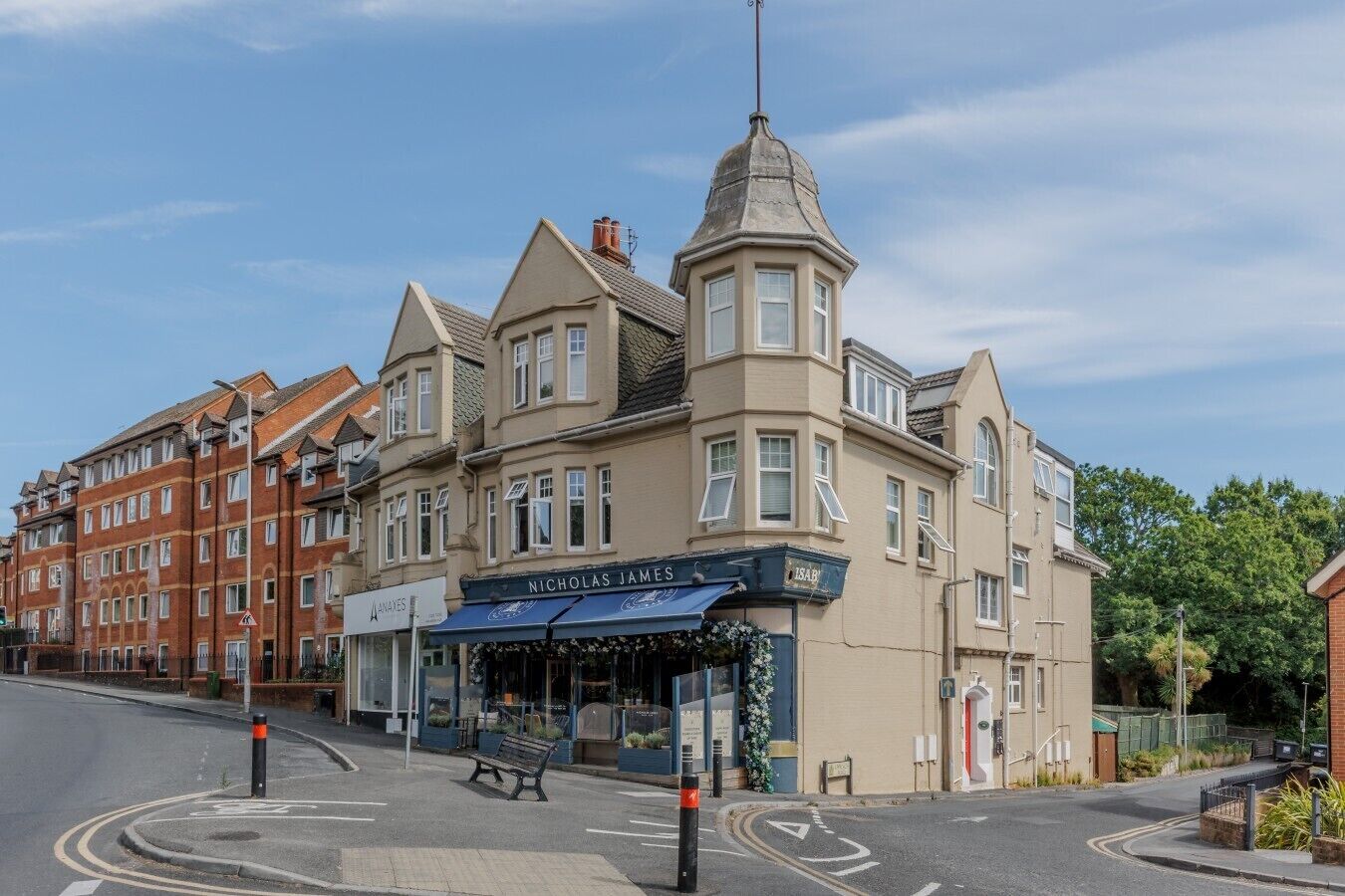 A corner building with a shop named 'Nicholas James' and a pub with outdoor seating.