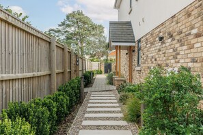 A narrow pathway flanked by a wooden fence and a brick wall, leading to a building with a dark roof. - The Laurels - Family space close to a choice of beaches (Poole)