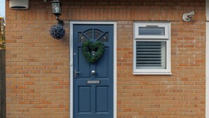 A blue door with a heart-shaped wreath, a window with blinds, and a brick wall. - Driftwood - Garden & parking close to beaches and town (Dorset)