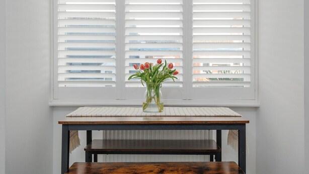 A table with a vase of flowers in front of a window with blinds. - Driftwood - Garden & parking close to beaches and town (Dorset)