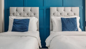 Two beds with tufted headboards, white bedding, and blue pillows against a blue wall. - Ocean Spray Suite - By the beaches, the seafront & town (Bournemouth)