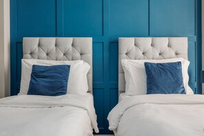 Two beds with tufted headboards, white bedding, and blue pillows against a blue wall. - Ocean Spray Suite - Within moments of beaches, the seafront & town (Bournemouth)