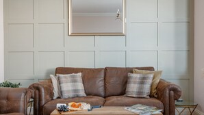 A brown leather sofa with plaid cushions, a wooden coffee table with a cheese board and magazine, and a wall-mounted mirror. - Ocean Spray Suite - By the beaches, the seafront & town (Bournemouth)
