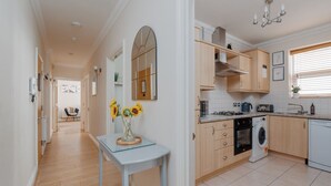 A modern kitchen with wooden cabinets, a built-in oven, a washing machine, and a dining area with a table and chairs. - Ocean Spray Suite - By the beaches, the seafront & town (Bournemouth)