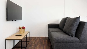 Ein modernes Wohnzimmer mit grauem Sofa, einem Flachbildfernseher, einem kleinen Holztisch mit einer Blumenkorb und einem Fischgrätparkettboden.