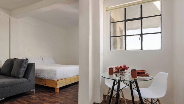 Ein Schlafzimmer mit einem Bett, einer Couch, einem Glastisch mit Stühlen und einem Fenster.