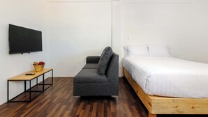 Ein Zimmer mit einer Couch, einem Bett, einem an der Wand befestigten Fernseher und einem kleinen Tisch mit einem Korb.
