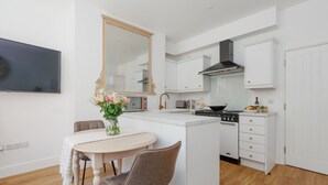 A modern kitchen with white cabinetry, a central island, a stove, and a dining area with a table and chairs. - Le Chambre d’Isabel - Close to shops, bars and places to eat & the beach (Dorset)