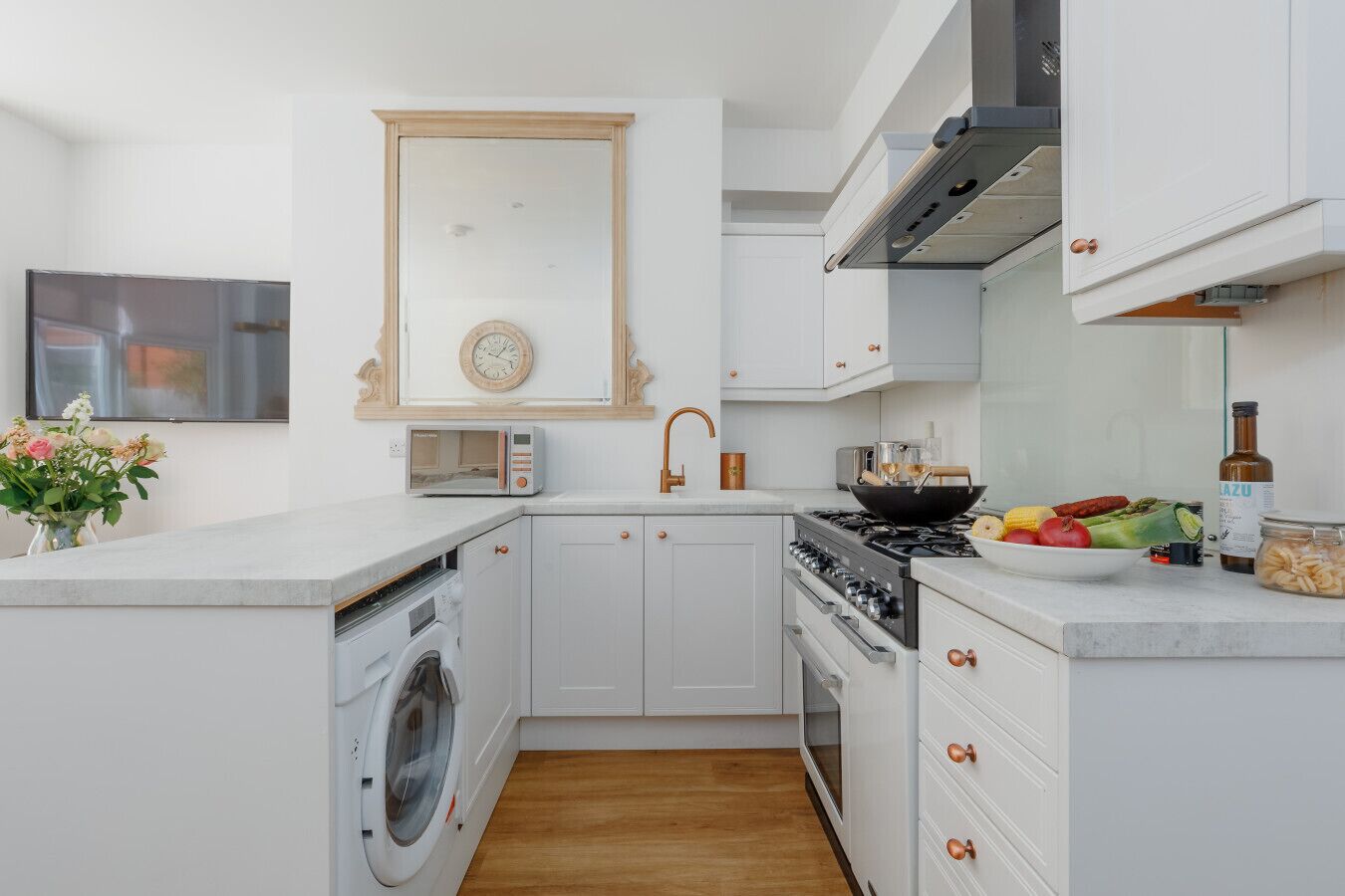 A modern kitchen with white cabinetry, a built-in washing machine, a stove, and a sink.