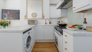 A modern kitchen with white cabinetry, a built-in washing machine, a stove, and a sink. - Le Chambre d’Isabel - Close to shops, bars and places to eat & the beach (Dorset)