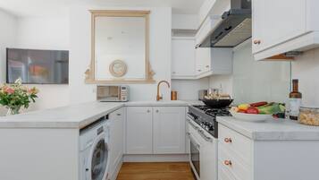 A modern kitchen with white cabinetry, a built-in washing machine, a stove, and a sink.