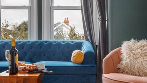 A room with a blue sofa, a wooden coffee table, a bottle of wine, and a plate of cheese and grapes. - Beaufort Heights - Well located for Christchurch and the beaches (Dorset)