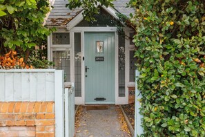 Ett hus med en ljusblå dörr, en tegelvägg och en liten trädgårdsyta.