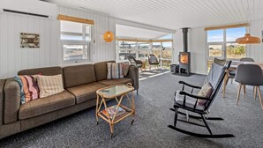 A spacious living area with a sofa, chairs, a glass coffee table, and a fireplace. - 4 Star Holiday Home in Lokken (Lokken)