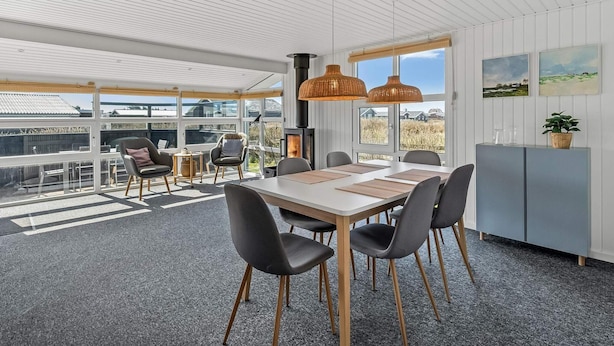 A modern dining area with a large table, chairs, and a view through large windows. - 4 Star Holiday Home in Lokken (Lokken)